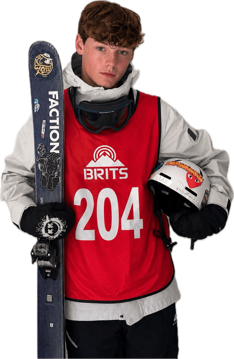 Finlay Kavanagh in a red BRITS competition bib, holding skis and a helmet